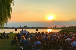 Blick über die Zuschauermenge zur Bühne bei der Lesung am Strand, mit der untergehenden Sonne, die sich im Inselsee spiegelt.