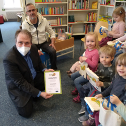 Die Kindergruppe aus dem „Butzemannhaus“ mit Leiter Mario Lüders hält die eben verteilten Lesestart-Beutel und Bibliotheksmitarbeiter Tilmann Wesolowski präsentiert die Urkunde für die Bibliothek. Foto: © Barlachstadt Güstrow