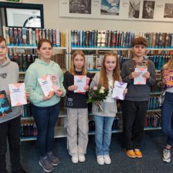 Gruppenfoto der Schulsieger aus dem Raum Güstrow mit der Gewinnerin des Vorlesewettbewerbs in der Bibliothek in der Mitte