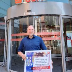 Bibliotheksverantwortlicher Tilmann Wesolowski mit der Förderurkunde in der Hand vor dem Eingang der OSPA-Zentrale in Rostock