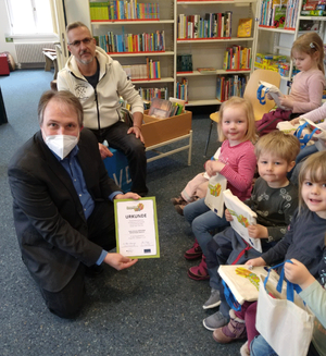 Die Kindergruppe aus dem „Butzemannhaus“ mit Leiter Mario Lüders hält die eben verteilten Lesestart-Beutel und Bibliotheksmitarbeiter Tilmann Wesolowski präsentiert die Urkunde für die Bibliothek. Foto: © Barlachstadt Güstrow