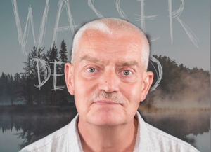Kopfbild vom Autor Siebo Woydt vor dem Buchcover, das einen sich im See spiegelnden Wald mit Restnebel zeigt.