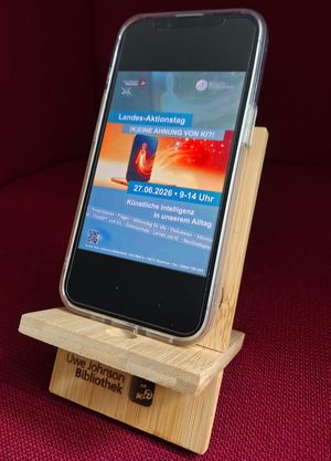 Ein Smartphone steht auf einem der Handyhalter, die man mit Quizrallye gewinnen kann, und auf dem Display ist das Plakat zur Veranstaltung zu sehen