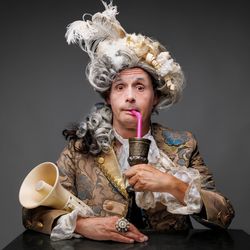 Philipp Weber mit Barocker Perrücke und Wams, im Arm ein Megaphon und an einen rosa Strohhalm aus einem Kupferbecher trinkend; (c) S. Büttner