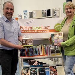 Maren Gläser vom Wildpark MV und Dr. Tilmann Wesolowski von der Bibliothek vor dem Regal des Ferienleseclubs FLL