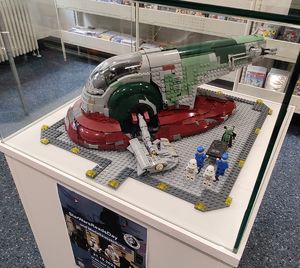 Vitrine in der Bibliothek mit einem Lego-Modell der Szene aus dem Star Wars Film Teil V, der Verschleppung von Han Solo durch den Kopfgeldjäger Boba Fett
