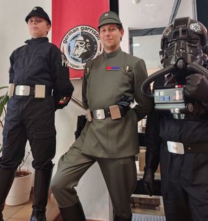 Drei Kostümträger, als imperiale Offiziere und Shadowtrooper kostümiert, stehen in der Bibliothek vor einem Banner mit dem Logo des Kostümclubs 501st German Garrison