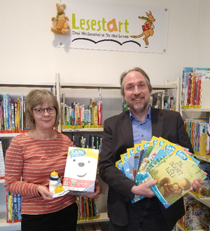 Birgit Hartleben und Tilmann Wesolowski von der Bibliothek präsentieren vor dem Lesestart-Regal den SAMi-Lesebären und dazugehörige Bilderbücher