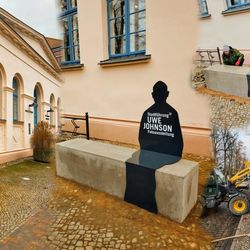 Bilder vom Ankranen des Betonblocks mit einem Gabelstapler, Anbringen der Stahlfigur und der fertigen Bank vor der Bibliothek